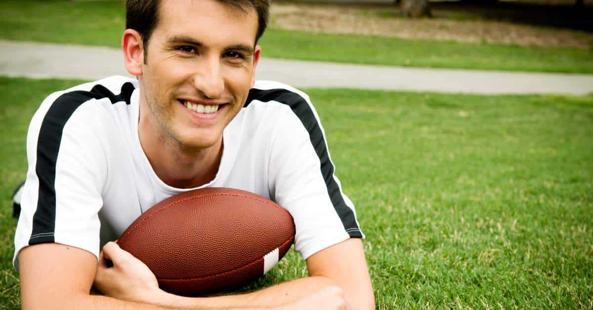 Student laying on his stomach on a football field while holding a football