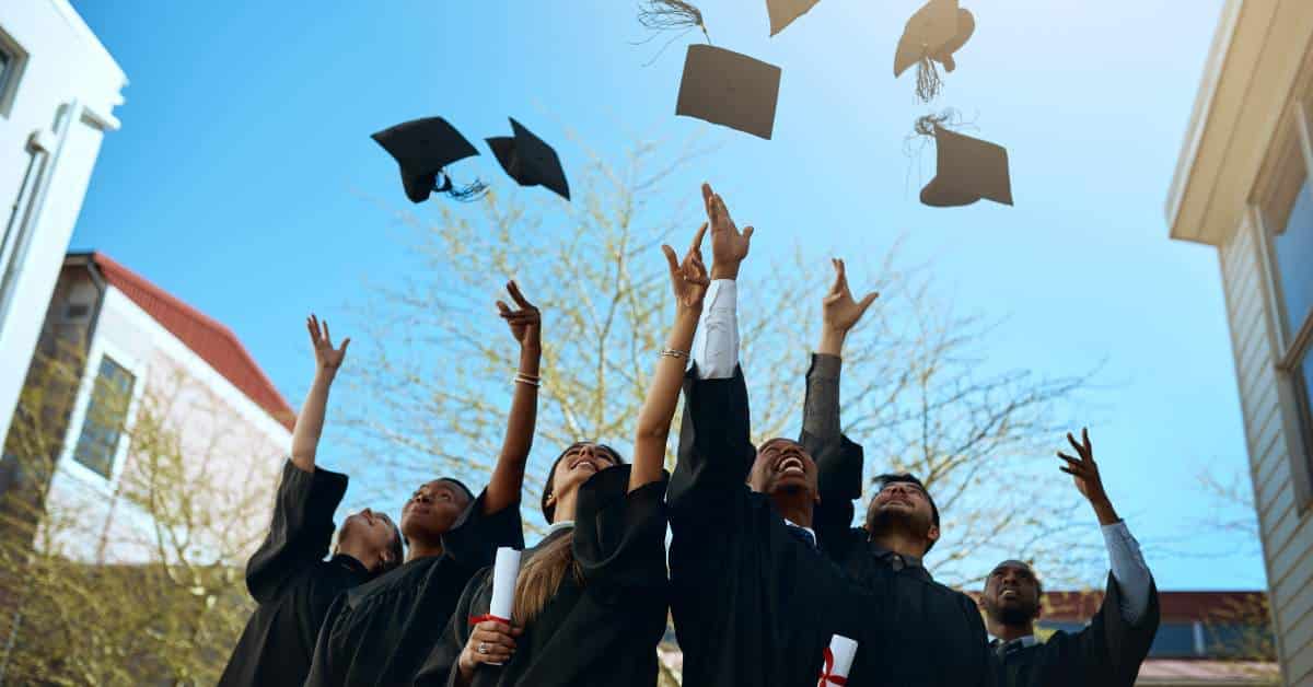College graduates looking up at the sky and throwing their graduation caps in the air