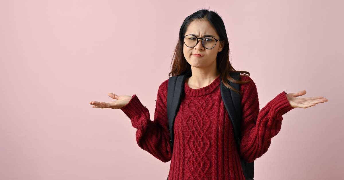College-aged female wearing a burgundy sweater holding her arms out and palms up in confusion