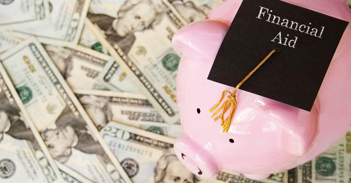 Money spread across a table with a pink piggy bank on top wearing a black mortar board that reads "Financial Aid."