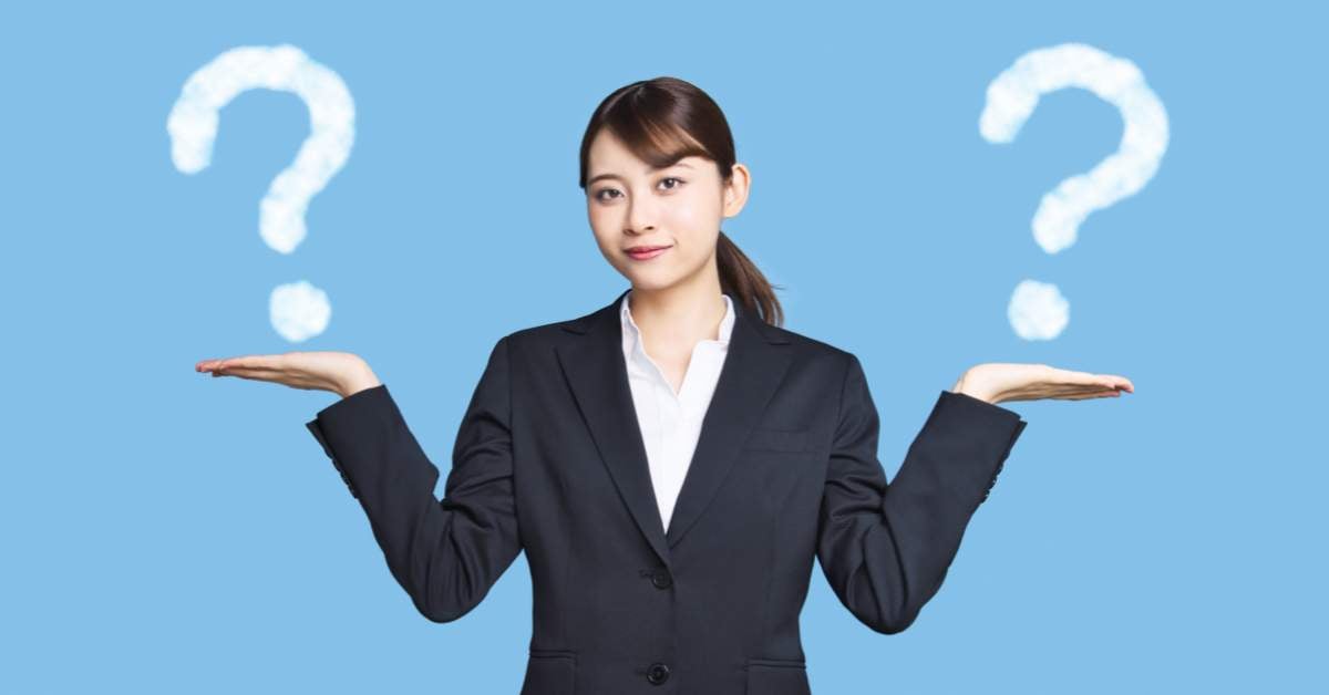 Asian woman in a black suit holds out both her hands, palms up. On each hand is a white question mark