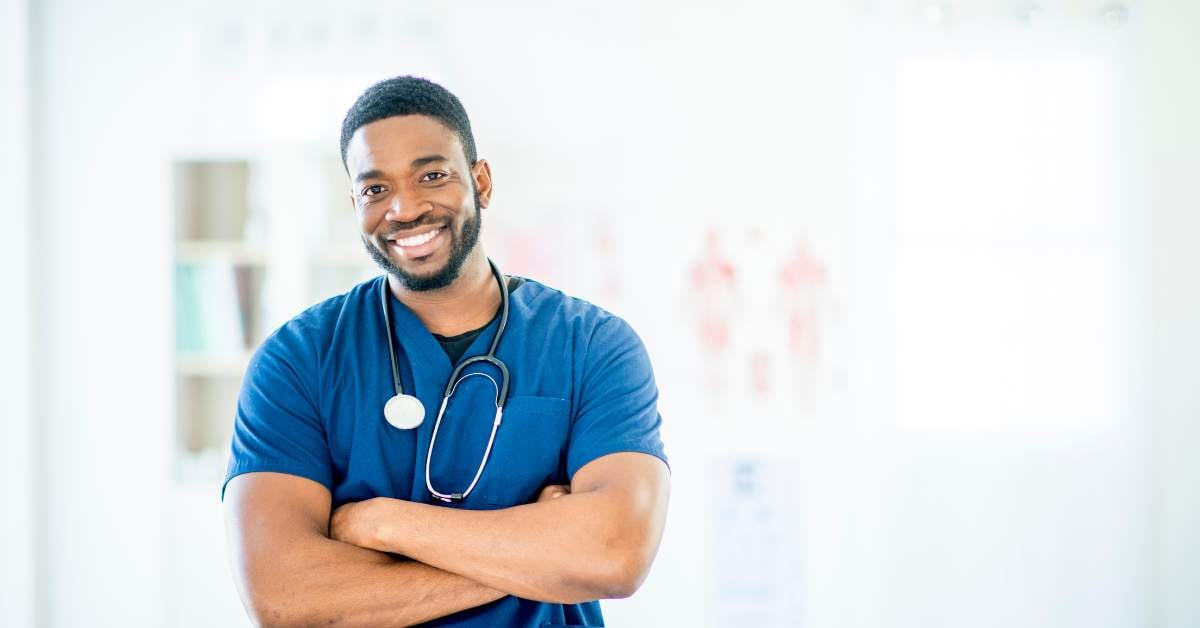 African American male smiling and wearing blue scrubs with a stethoscope around his neck