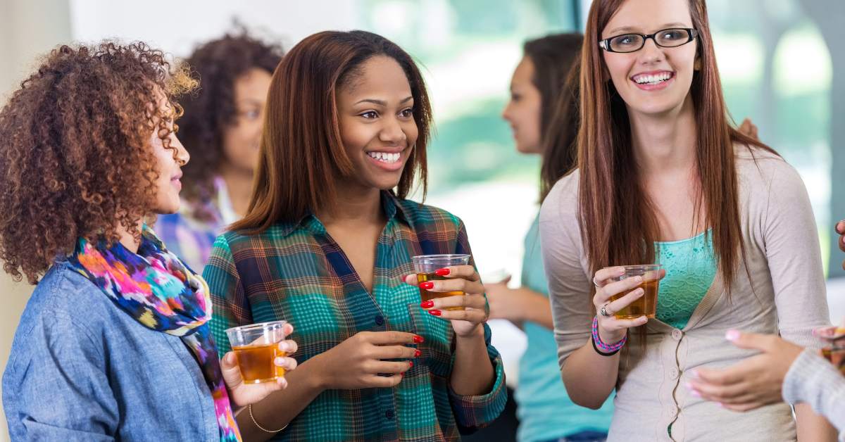 Three college aged girls talking to and smiling at someone who is outside of the photo area