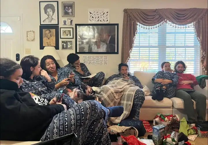 A large family in matching pajamas sitting on two couches and talking animatedly.