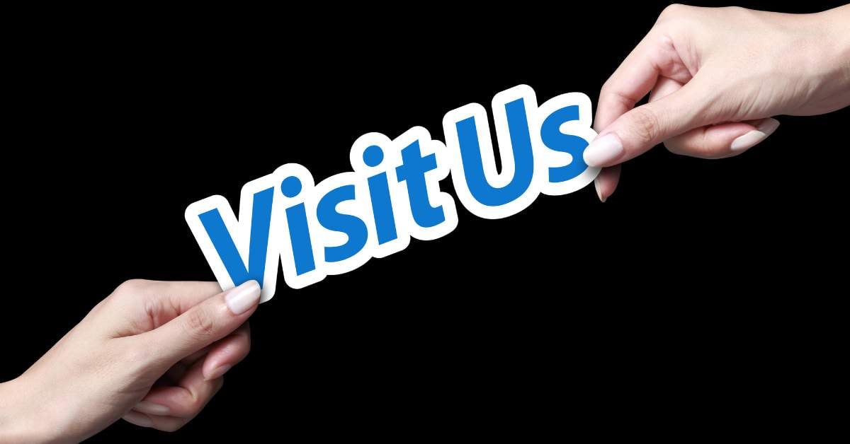 A sign that says "Visit Us" with a hand holding each side of it.