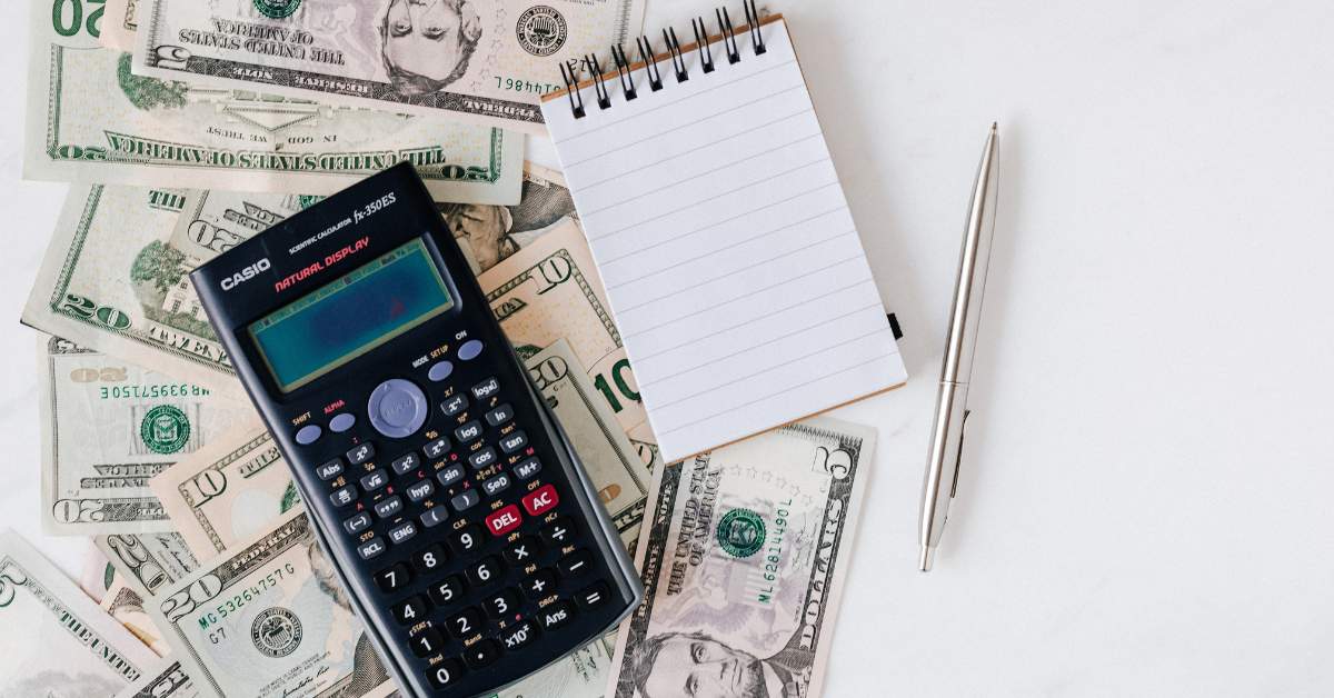 money on a table with a calculator, pen, and paper on top of it